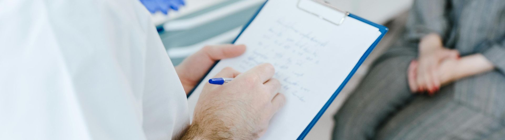Medical professional writing patient notes on clipboard during consultation.